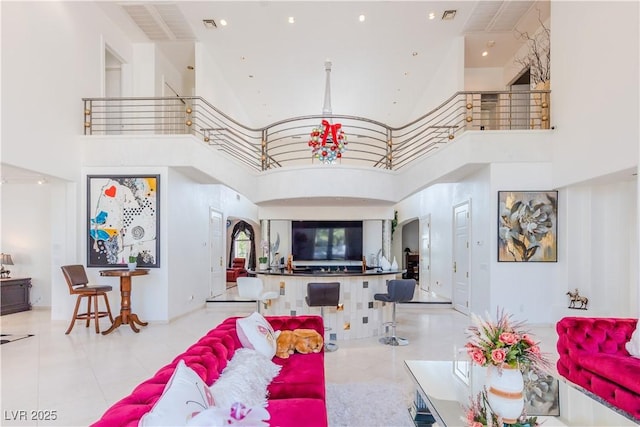 tiled living room featuring arched walkways, a towering ceiling, visible vents, and an inviting chandelier