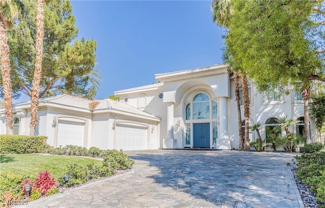 mediterranean / spanish-style house with decorative driveway, an attached garage, a tile roof, and stucco siding