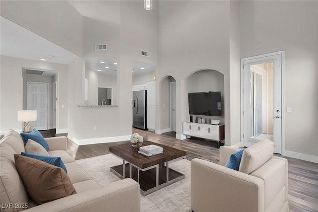 living room with arched walkways, wood finished floors, visible vents, and baseboards