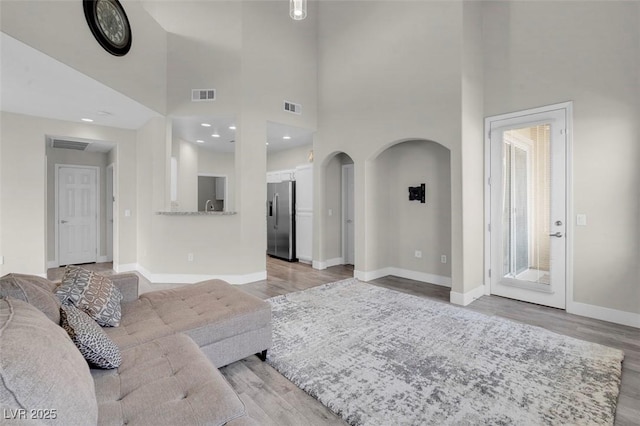 living room with arched walkways, baseboards, visible vents, and light wood-type flooring