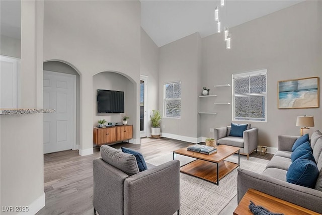 living room with light wood-type flooring, baseboards, and high vaulted ceiling