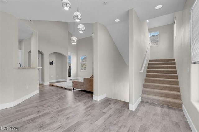 stairway with arched walkways, a healthy amount of sunlight, baseboards, and wood finished floors