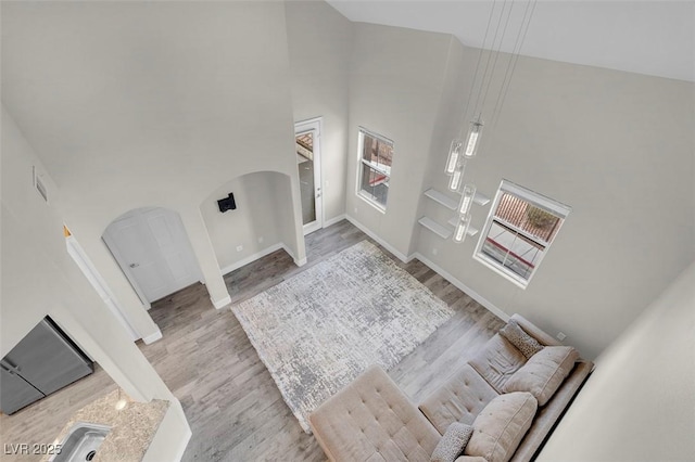 foyer featuring wood finished floors, arched walkways, a towering ceiling, and baseboards