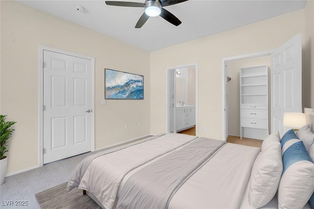 bedroom with a ceiling fan, baseboards, a walk in closet, light colored carpet, and connected bathroom