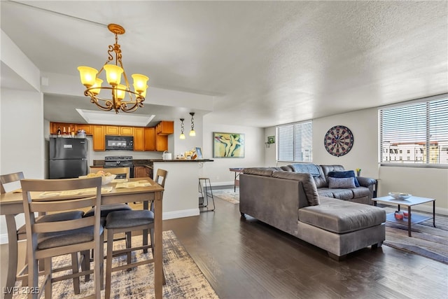 living room featuring dark wood-style floors, a textured ceiling, a chandelier, and baseboards