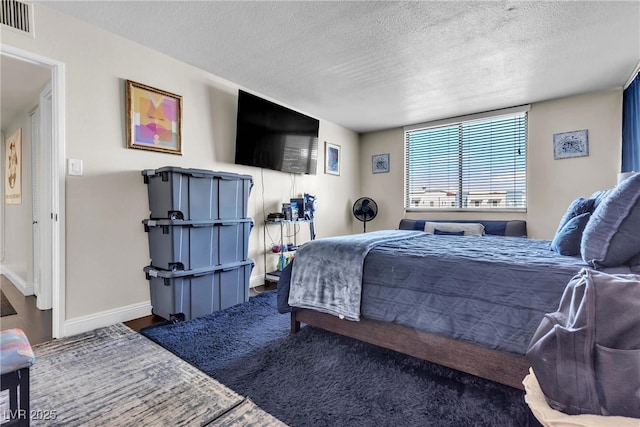 bedroom with a textured ceiling, wood finished floors, visible vents, and baseboards