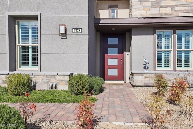 view of exterior entry featuring stone siding and stucco siding