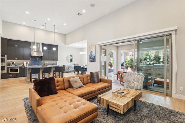 living room featuring a high ceiling, light wood-type flooring, visible vents, and a ceiling fan