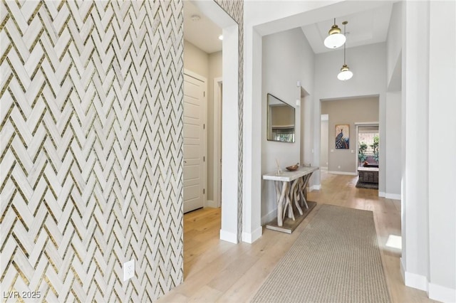 hall featuring an accent wall, light wood-type flooring, baseboards, and a high ceiling