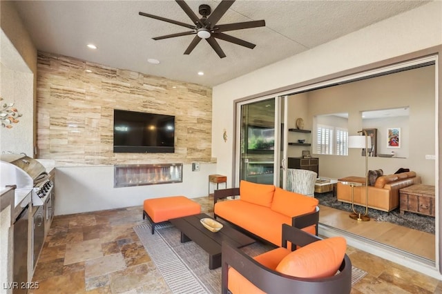 living area with a tiled fireplace, a ceiling fan, stone finish flooring, a textured ceiling, and recessed lighting