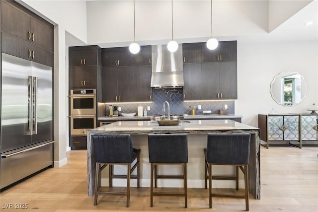 kitchen with stainless steel appliances, tasteful backsplash, wall chimney exhaust hood, and a kitchen bar