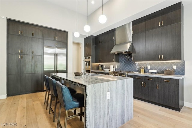 kitchen featuring light wood-type flooring, wall chimney range hood, pendant lighting, and backsplash