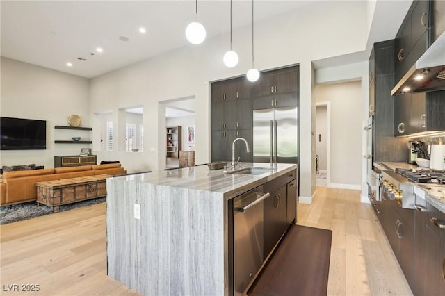 kitchen featuring wall chimney exhaust hood, light wood-style flooring, light stone countertops, stainless steel appliances, and a sink