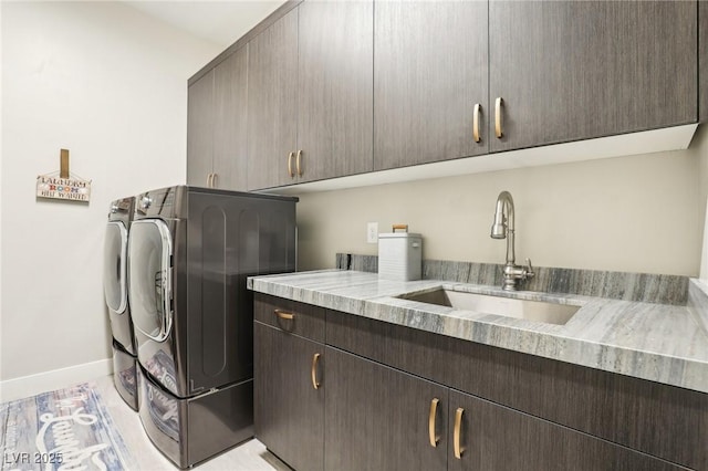 laundry room featuring washing machine and clothes dryer, a sink, cabinet space, and baseboards