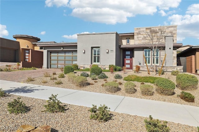 modern home with a garage, stone siding, decorative driveway, and stucco siding