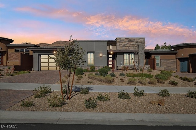 contemporary home featuring decorative driveway, stone siding, an attached garage, and stucco siding