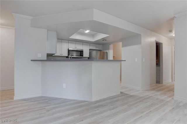 kitchen with dark countertops, appliances with stainless steel finishes, light wood-type flooring, a peninsula, and baseboards