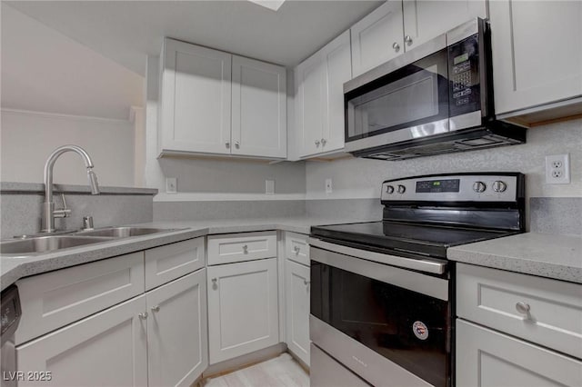 kitchen with white cabinets, ornamental molding, stainless steel appliances, light countertops, and a sink