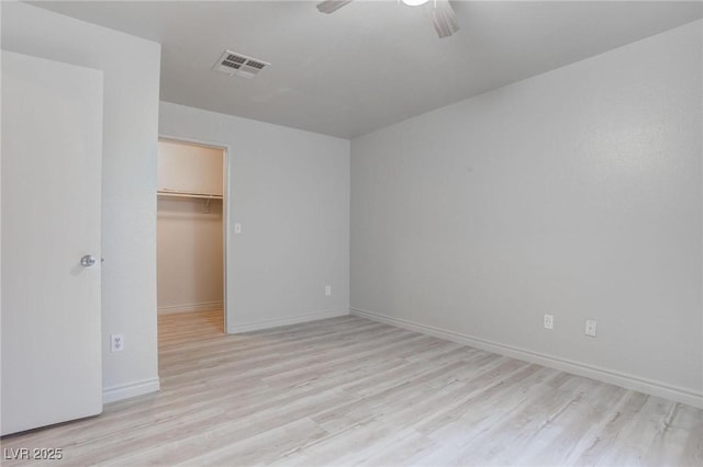 unfurnished bedroom featuring visible vents, a spacious closet, light wood-style floors, ceiling fan, and baseboards