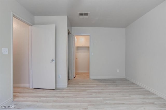 unfurnished bedroom featuring baseboards, visible vents, a walk in closet, and wood finished floors