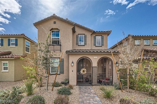 mediterranean / spanish-style home with a tile roof, fence, and stucco siding