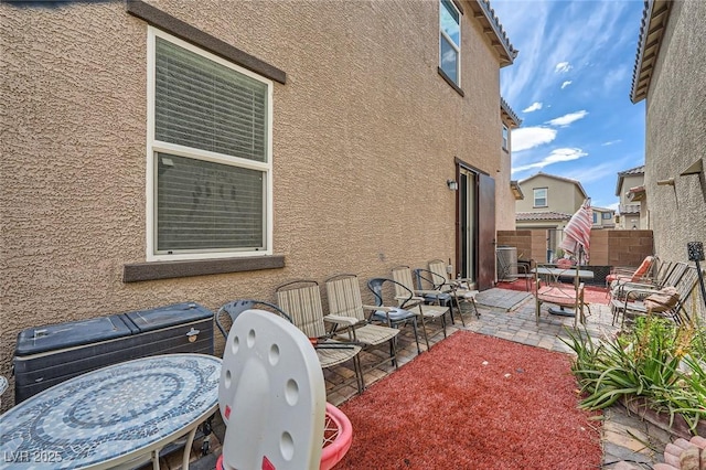 view of side of home with stucco siding, fence, central AC, and a patio