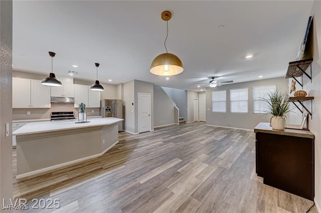 kitchen with under cabinet range hood, stainless steel appliances, white cabinets, light countertops, and light wood finished floors