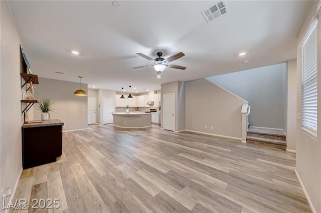 unfurnished living room with stairway, light wood-type flooring, visible vents, and a ceiling fan