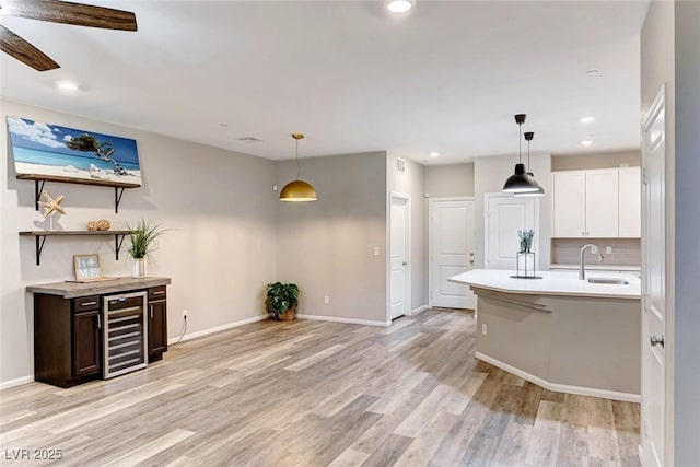 kitchen with light wood finished floors, beverage cooler, decorative backsplash, light countertops, and a sink