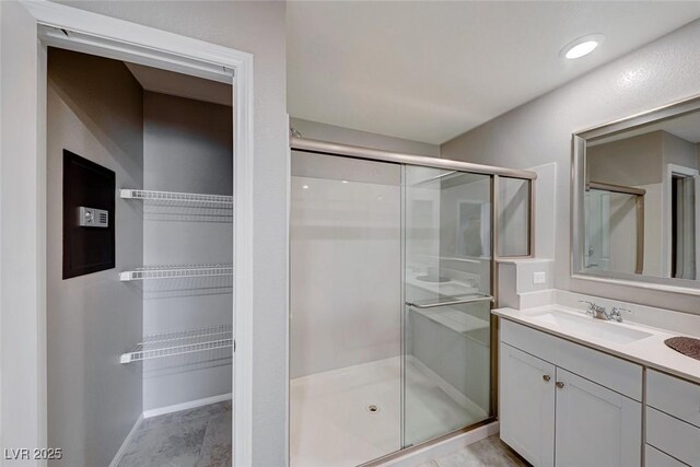 bathroom featuring a stall shower, vanity, baseboards, and a spacious closet