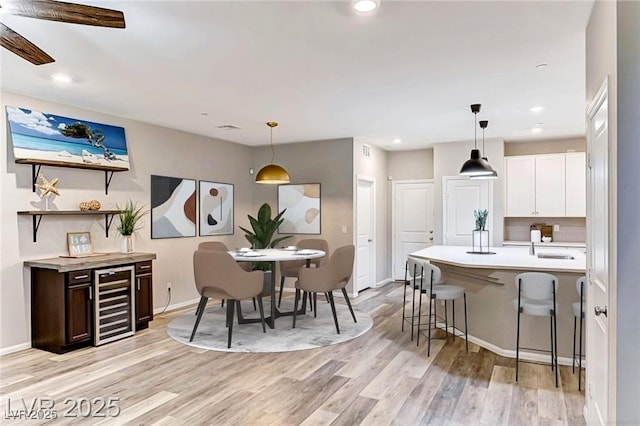 interior space featuring a breakfast bar, wine cooler, light wood-type flooring, and light countertops