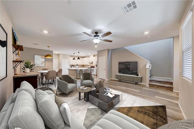 living area with baseboards, visible vents, a ceiling fan, stairs, and light wood-style floors