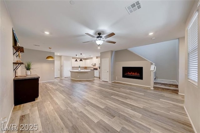 unfurnished living room with a warm lit fireplace, visible vents, ceiling fan, and light wood finished floors