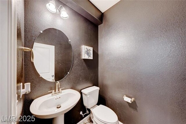 bathroom with a textured wall, a sink, and toilet