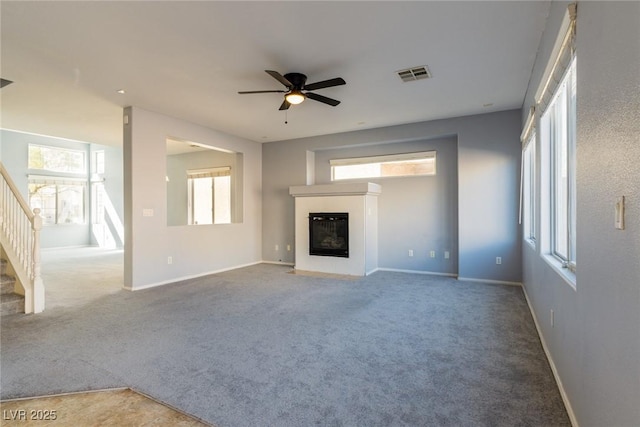 unfurnished living room featuring a glass covered fireplace, stairway, carpet, and visible vents