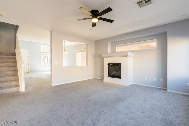 unfurnished living room featuring stairway, visible vents, carpet floors, a tile fireplace, and a wealth of natural light