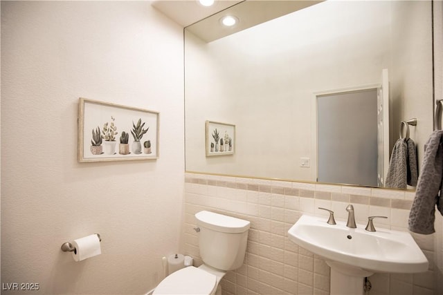 bathroom with toilet, a wainscoted wall, a sink, tile walls, and recessed lighting