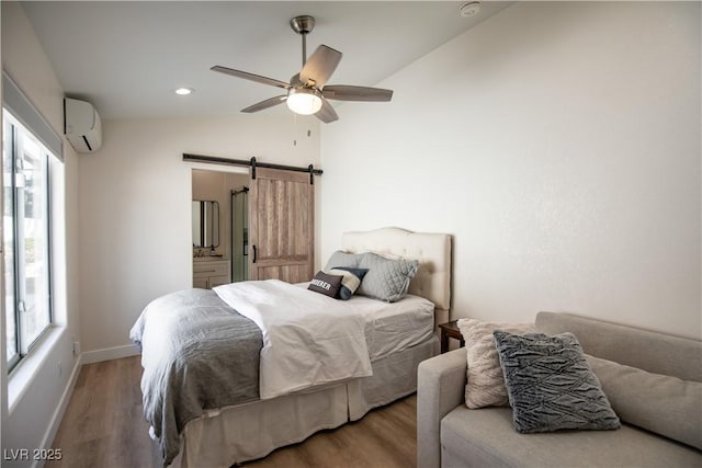 bedroom with a barn door, multiple windows, a wall unit AC, and wood finished floors