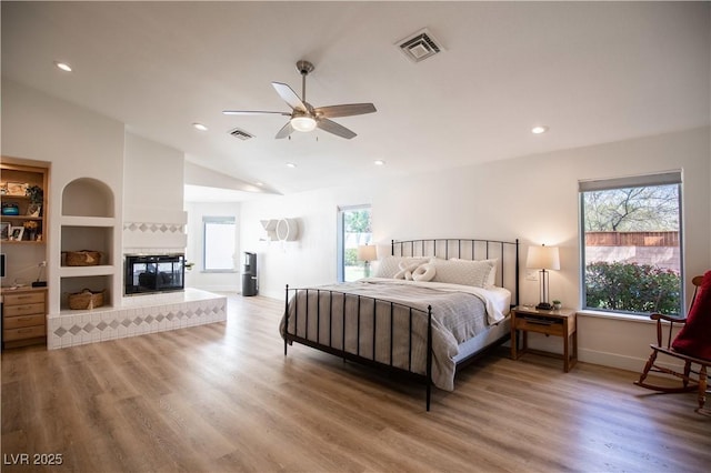 bedroom with light wood-style flooring, visible vents, vaulted ceiling, and a multi sided fireplace