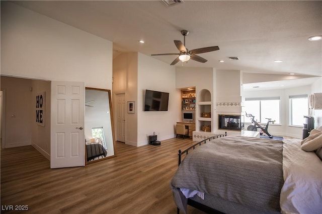 bedroom with lofted ceiling, wood finished floors, a multi sided fireplace, visible vents, and baseboards