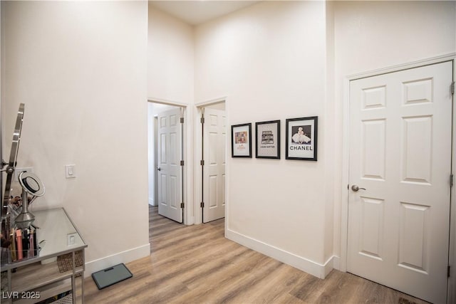 hallway with baseboards, a towering ceiling, and light wood finished floors