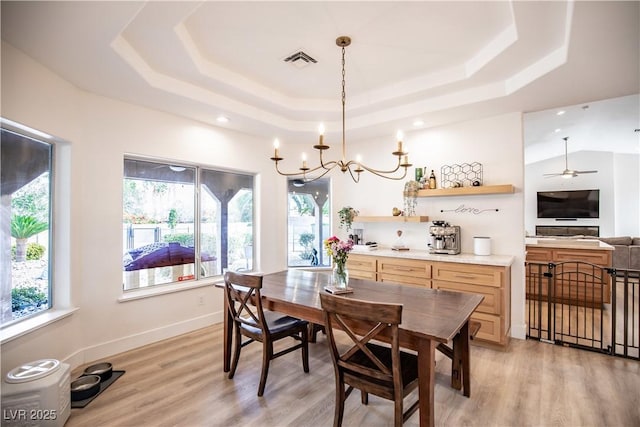 dining space with light wood-style floors, visible vents, a tray ceiling, and baseboards