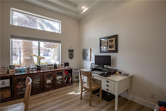 office area with a towering ceiling, light wood-style floors, and baseboards