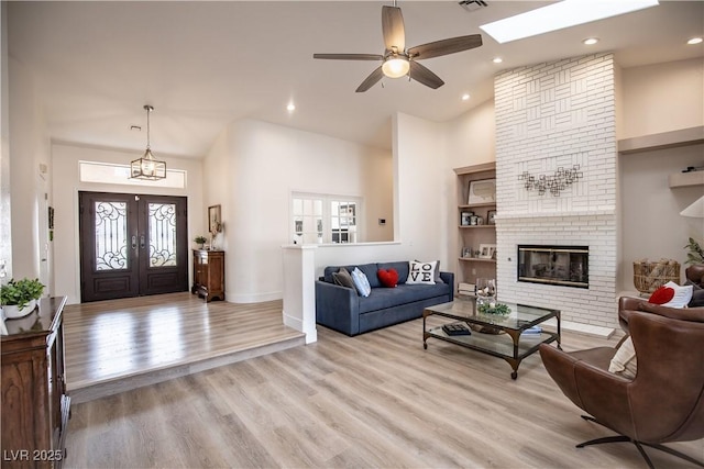 living room featuring visible vents, a towering ceiling, french doors, light wood-type flooring, and a brick fireplace