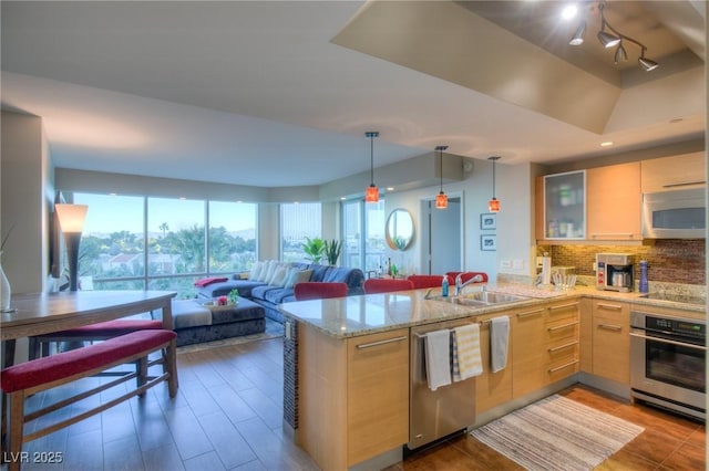 kitchen with tasteful backsplash, decorative light fixtures, a peninsula, stainless steel appliances, and a sink