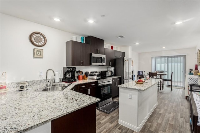 kitchen with visible vents, appliances with stainless steel finishes, a kitchen island, a sink, and wood finished floors