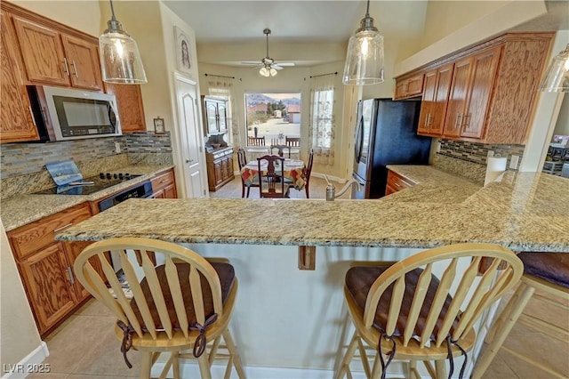 kitchen featuring a peninsula, appliances with stainless steel finishes, brown cabinetry, and light stone counters