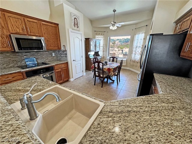 kitchen featuring brown cabinets, a sink, vaulted ceiling, stainless steel appliances, and backsplash