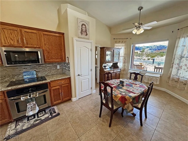 kitchen featuring brown cabinets, light tile patterned floors, stainless steel appliances, lofted ceiling, and tasteful backsplash