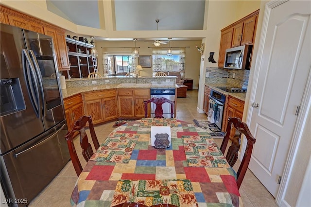 kitchen with appliances with stainless steel finishes, brown cabinets, a peninsula, a sink, and light tile patterned flooring